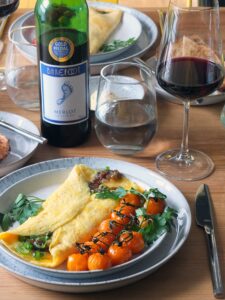 Image of a bacon jam omelette with a bottle of Barefoot merlot in the background.